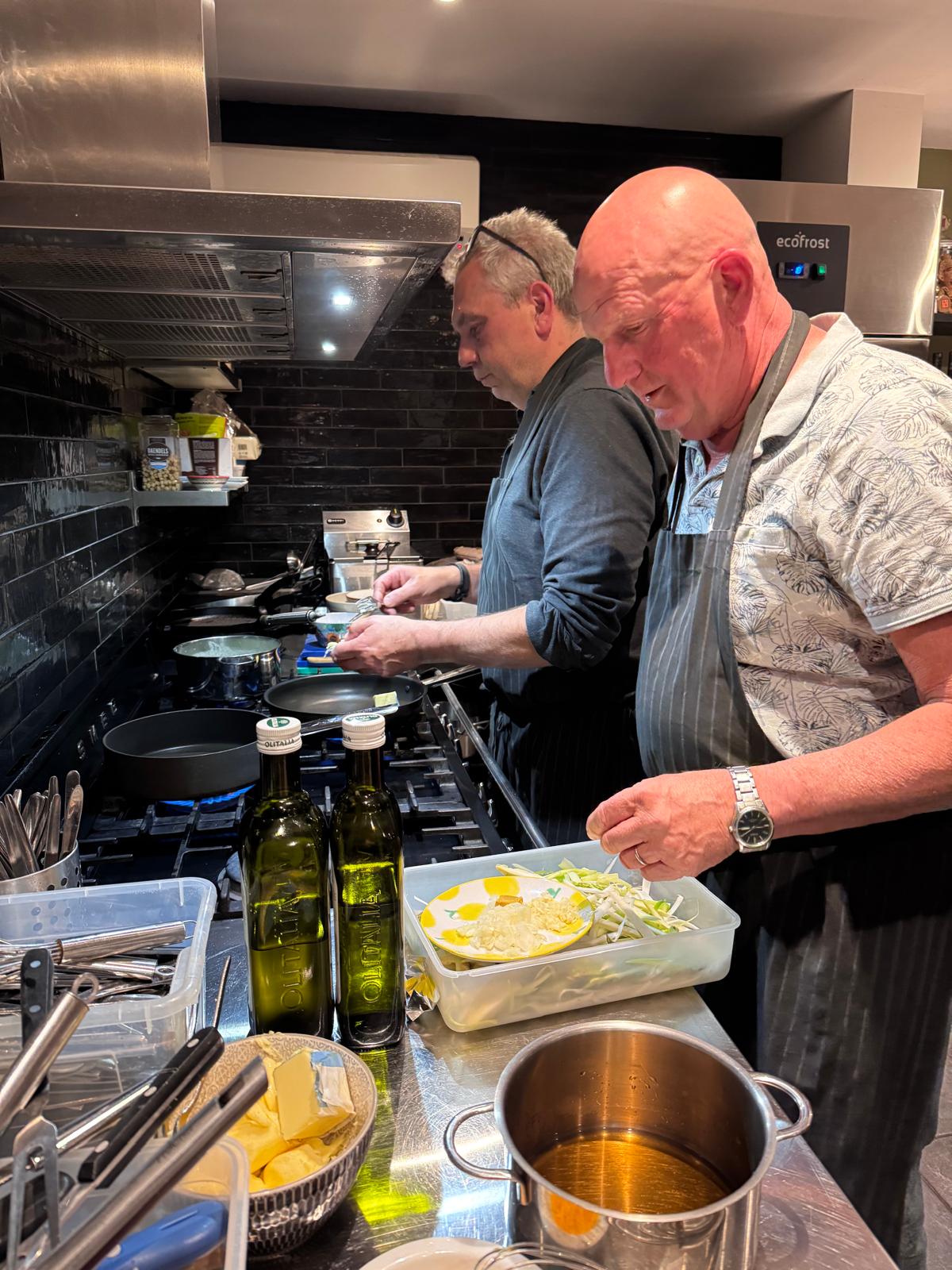 Twee kels in concentratie aan het fornuis, met flessen olijfolie op het werkblad.
