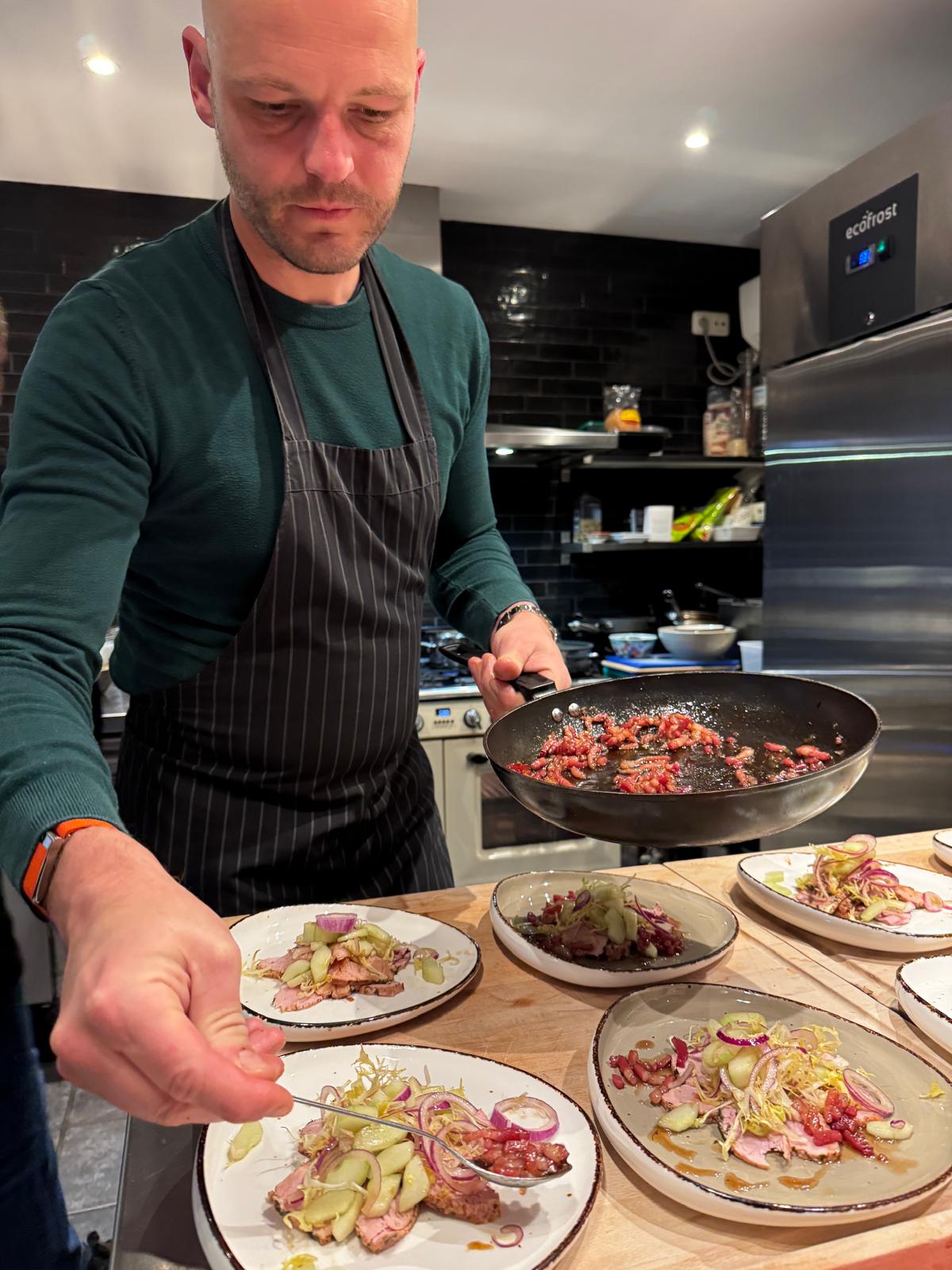 Een kel laat een pan met gefruite kruiden aan de borden zien.